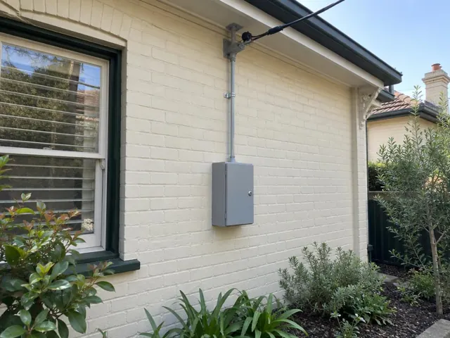Overhead service cable and point-of-attachment bracket on a brick house wall in Cammeray